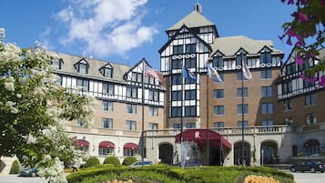 A large hotel with a prominent tower, multiple flags, and a well-maintained garden with flower beds.