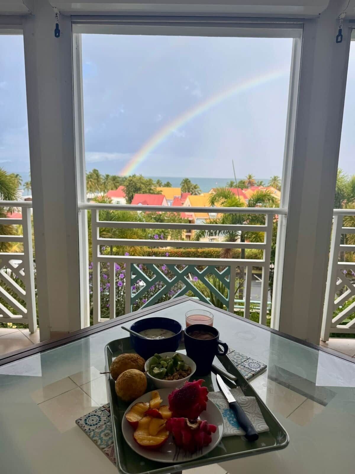 A balcony with a table set for breakfast, a glass of juice, and a plate of fruit and eggs.