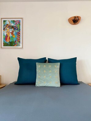 Ein Bett mit türkisblau-grüner Bettwäsche und einem Kopfkissen mit Palmenmotiven.