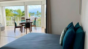 Ein Schlafzimmer mit Bett, Kissen, einem Nachttisch, einer Lampe und Blick auf einen Balkon mit Tisch und Stühlen.