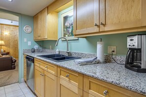 A kitchen with wooden cabinets, a granite countertop, a dishwasher, a coffee maker, and a clock on the wall. - Steps to the Slopes! Breck Ski Condo w/ Fireplace (Breckenridge)