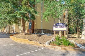 A building with a sign labeled 'COLUMBINE' surrounded by trees and a landscaped area with mulch and rocks. - Steps to the Slopes! Breck Ski Condo w/ Fireplace (Breckenridge)