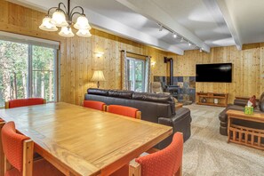 A spacious living room with a wooden dining table, leather sofa, and a flat-screen TV mounted on the wall. - Steps to the Slopes! Breck Ski Condo w/ Fireplace (Breckenridge)