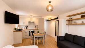 Un apartamento moderno con kitchenette, comedor, sala de estar con sofá y televisor de pantalla plana montado en la pared.