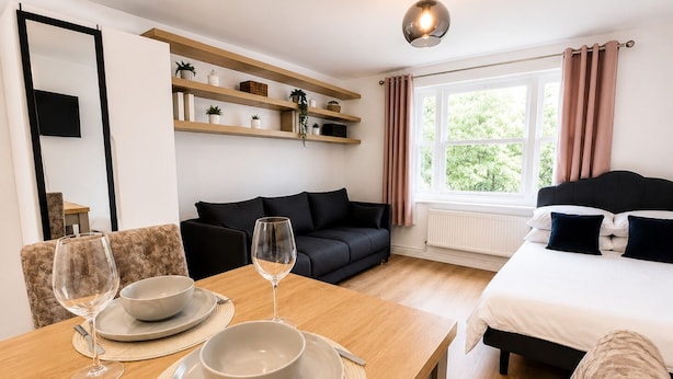 Una habitación moderna con una mesa de comedor preparada para dos personas, un sofá, una cama y una ventana con cortinas.