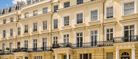 A row of yellow townhouses with white trim, multiple windows, and black wrought iron balconies.