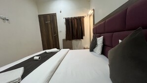 Una habitación de hotel con cama, mesita de noche, puerta de madera y ventana con cortinas.