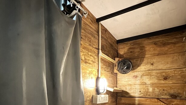 Una habitación con cama, cortina, lámpara fijada a la pared y cabecera de madera.
