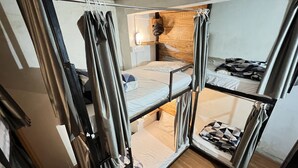 Habitación con literas compactas de varios niveles, cabecera de madera, una mesita pequeña y una lámpara fijada a la pared.