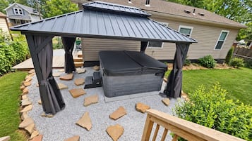 A covered outdoor seating area with a bench and a table, surrounded by a gravel path and a wooden deck.
