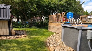 Un cortile con un canestro da basket, un patio in legno e un capanno.