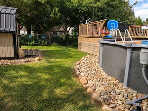 A backyard with a basketball hoop, a wooden deck, and a shed.