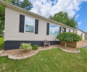 A single-story mobile home with a front porch, a small garden, and a satellite dish. - The Oasis of Massillon Pet Friendly + Pool + Fenced in Back Yard (Massillon)
