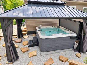 A hot tub under a covered pavilion with a pergola structure, surrounded by gravel and stone. - The Oasis of Massillon Pet Friendly + Pool + Fenced in Back Yard (Massillon)