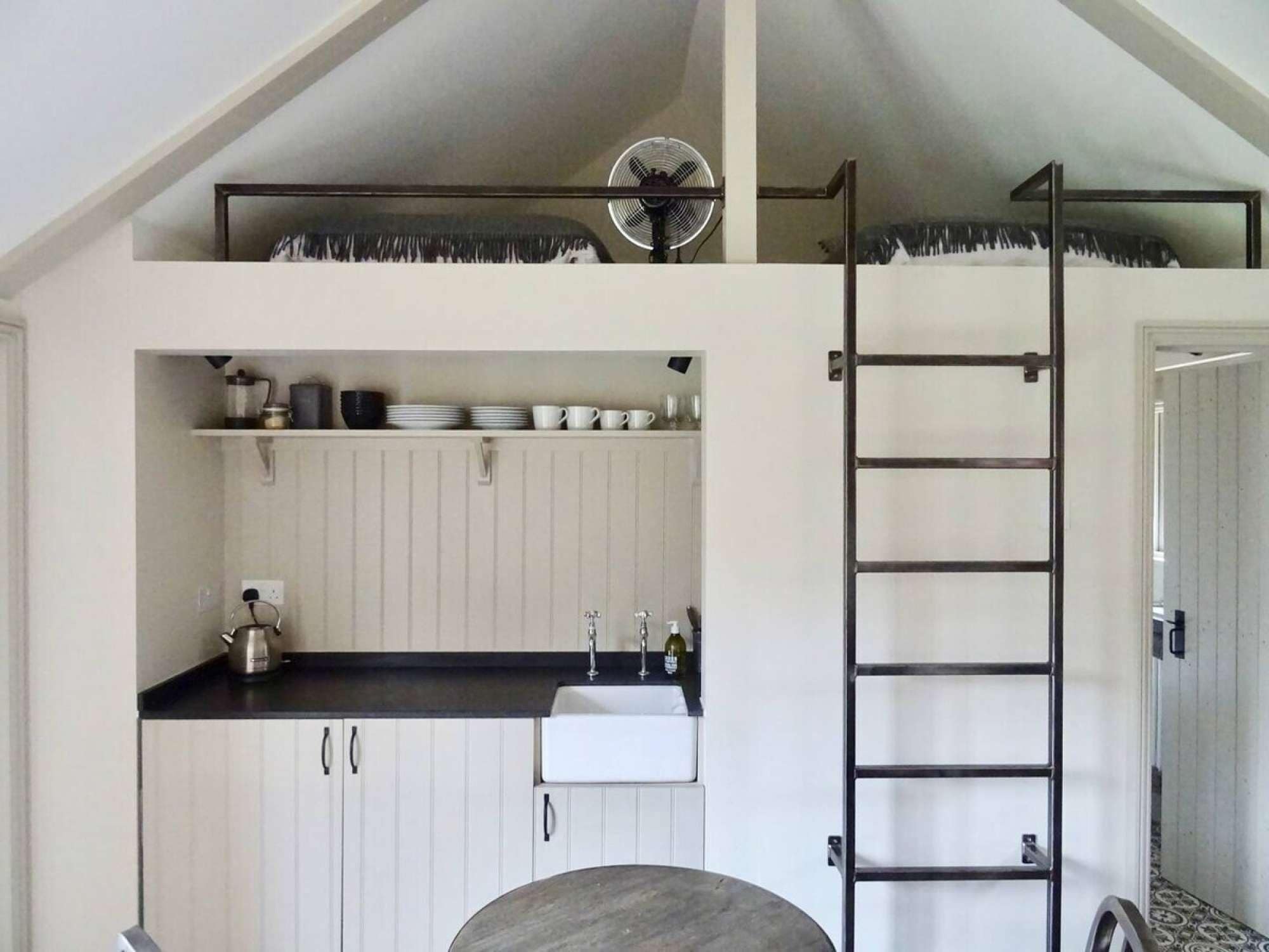 A compact kitchen with a lofted sleeping area, a sink, and a ladder.