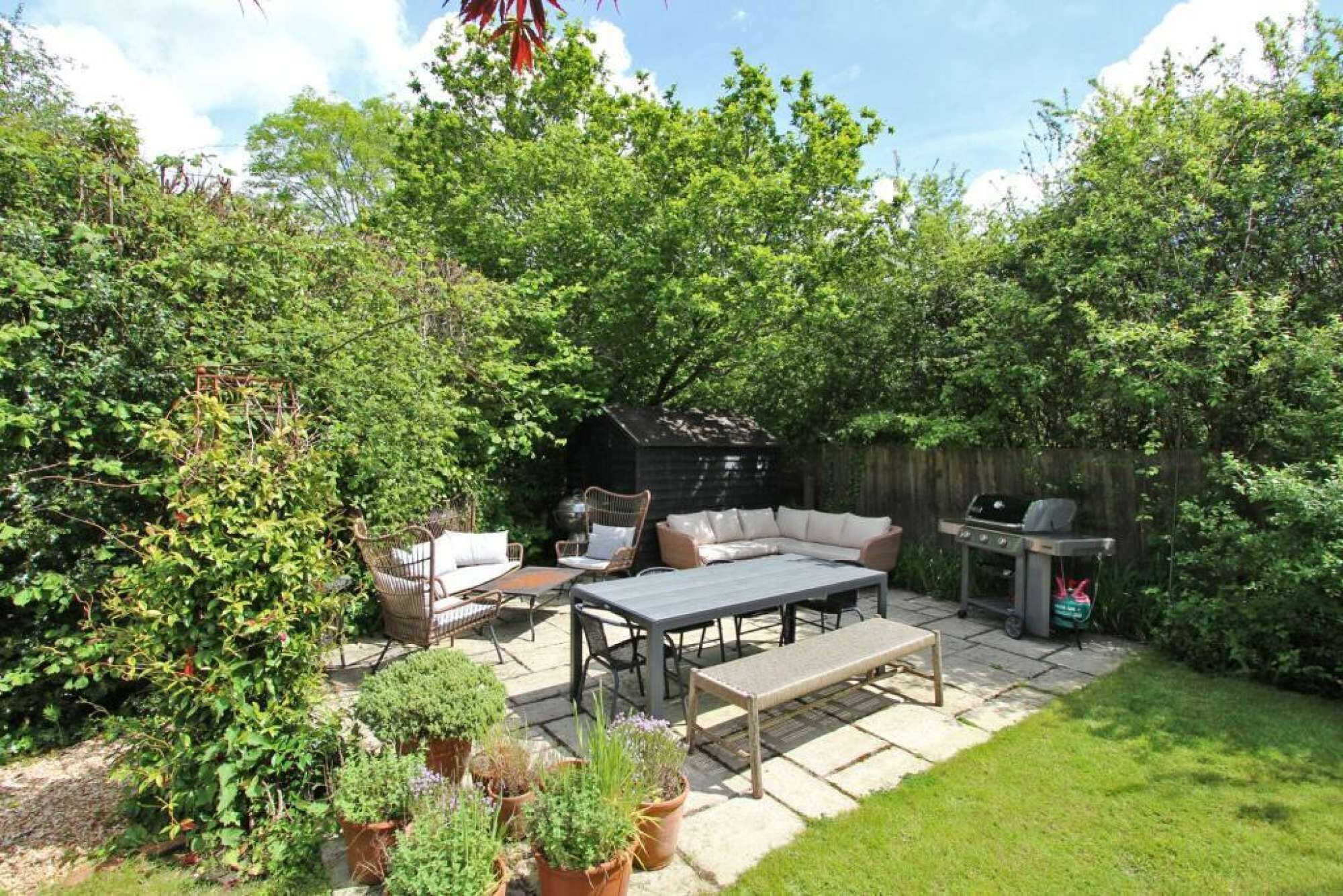 An outdoor patio area with a seating arrangement, a grill, and potted plants.