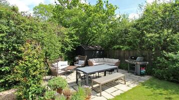 An outdoor patio area with a seating arrangement, a grill, and potted plants.