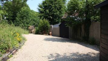 A gravel driveway leading to a wooden gate, surrounded by dense greenery and a wooden fence.