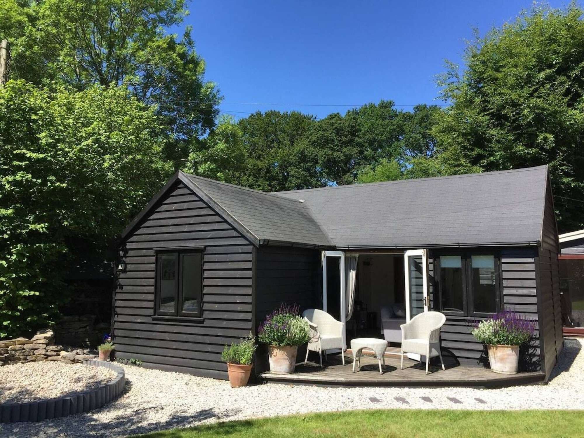 A black wooden house with a porch, white chairs, and potted plants.