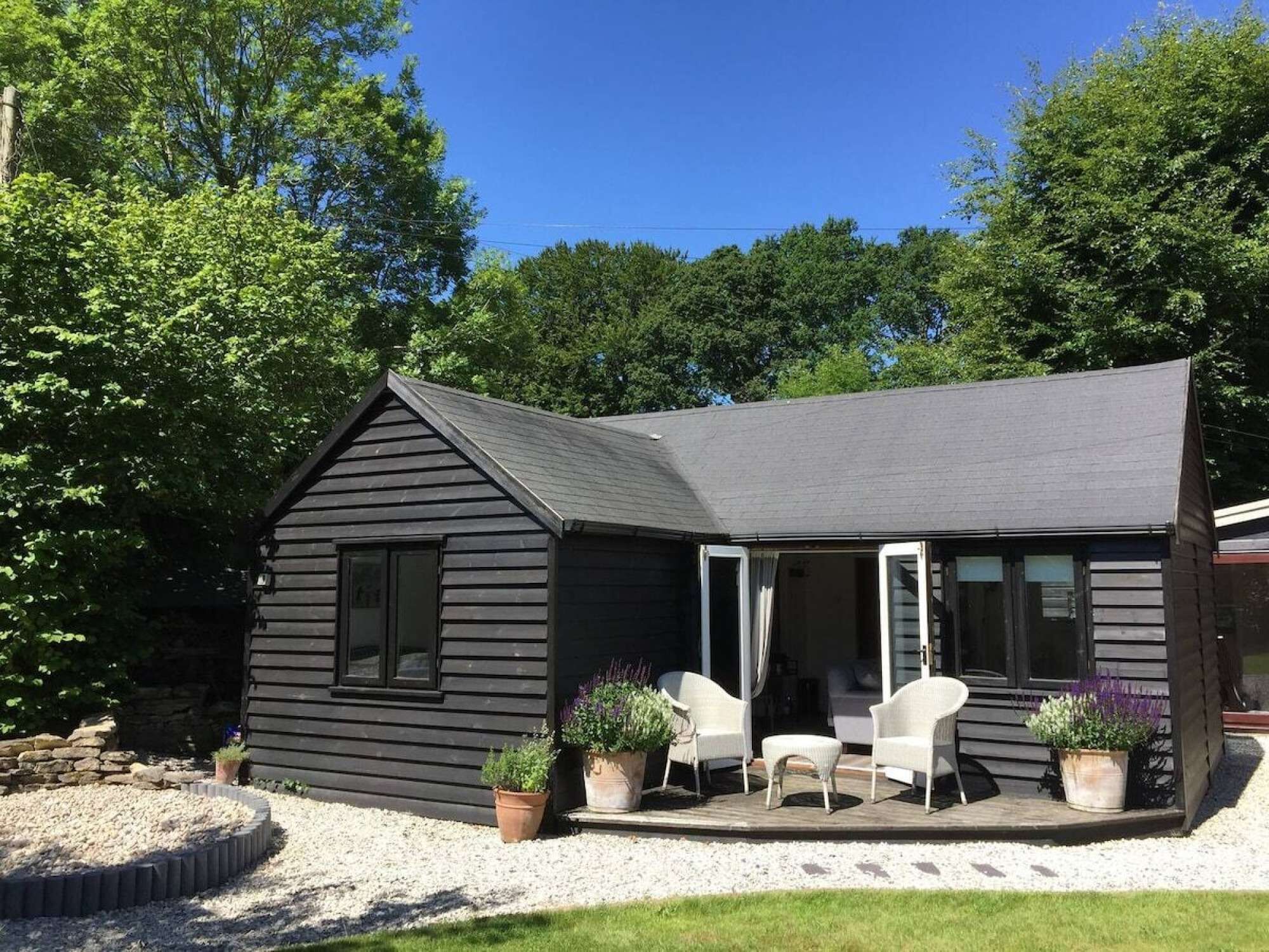 A black wooden house with a porch, white chairs, and potted plants.