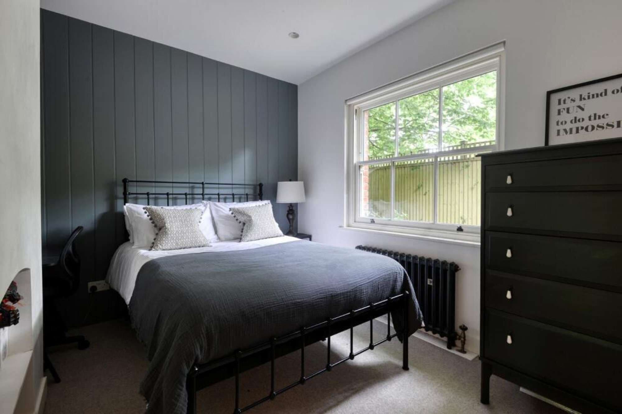 A bedroom with a bed, a dresser, a window, and a radiator.