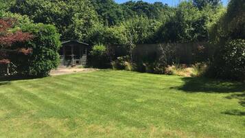 A well-maintained grassy yard with a wooden structure, surrounded by dense foliage and a wooden fence.