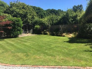A well-maintained grassy yard with a wooden structure, surrounded by dense foliage and a wooden fence. - Railway Junction Cottage AND The Cabin (Brockenhurst)