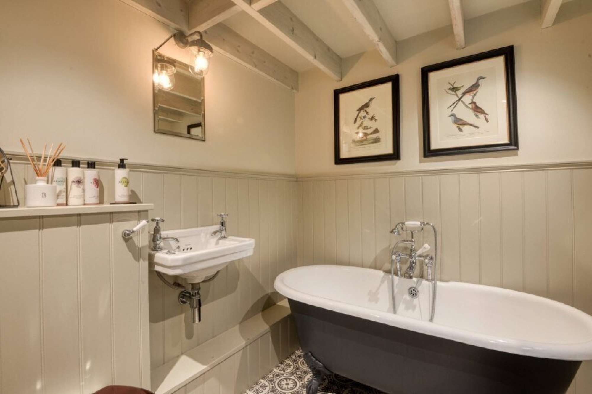 A bathroom with a white sink, a black bathtub, and two framed bird illustrations on the wall.