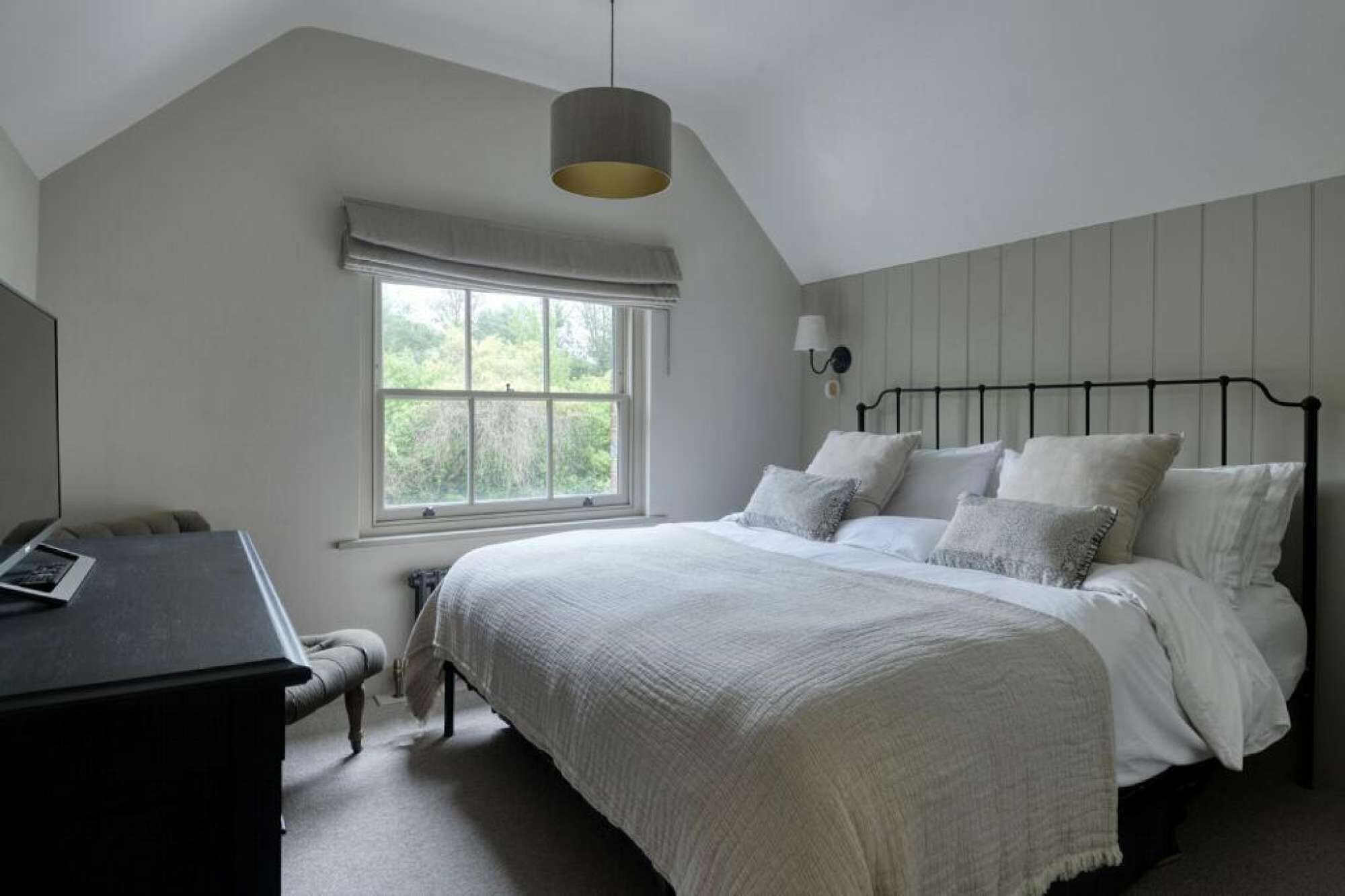 A bedroom with a bed, a desk, a window, and a hanging light fixture.