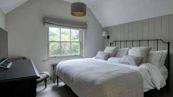 A bedroom with a bed, a desk, a window, and a hanging light fixture.
