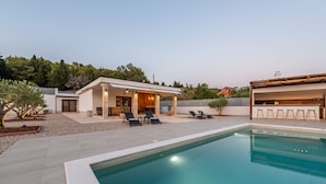 Ein moderner Poolbereich im Freien mit überdachter Terrasse, Liegestühlen und einem klaren, blauen Pool.
