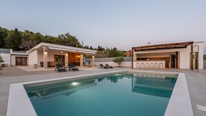 Ein moderner Poolbereich mit rechteckigem Pool, Gartenmöbeln und einer überdachten Terrasse.