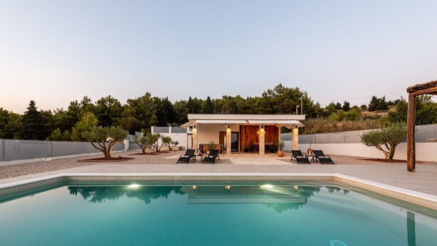 Ein moderner Poolbereich mit klarem Pool, Liegestühlen und einem Gebäude mit offener Terrasse.