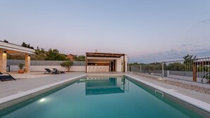 Ein Schwimmbad mit einer Sonnenterrasse, Liegestühlen und einem überdachten Sitzbereich.