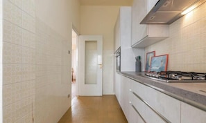 Cocina estrecha con baldosas blancas estampadas, estufa a gas y una puerta que da a otra habitación.