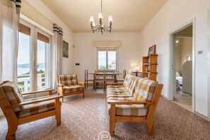A room with a sofa, two armchairs, a dining table, and a chandelier.