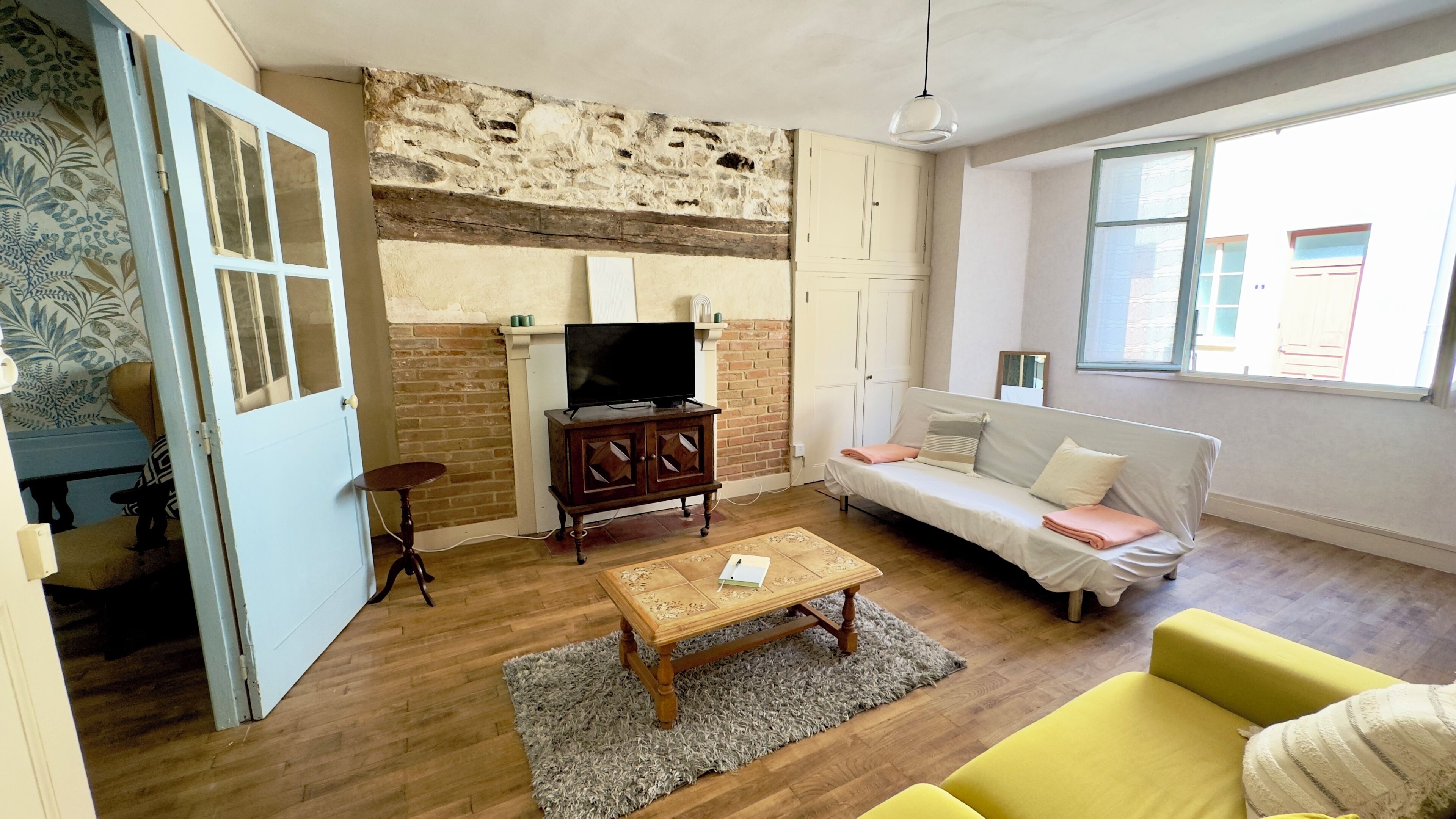 Una sala de estar con pared de ladrillo, muebles de madera, un sofá, un sillón amarillo y un televisor.