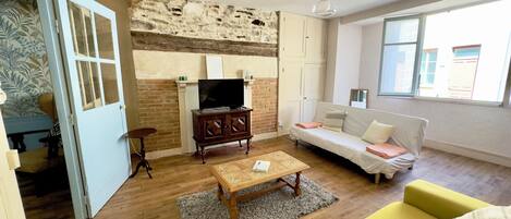 Una sala de estar con pared de ladrillo, muebles de madera, un sofá, un sillón amarillo y un televisor.