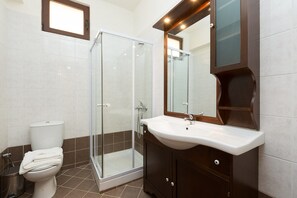 Une salle de bain avec une douche à parois de verre, des toilettes blanches et un meuble-lavabo en bois foncé avec un lavabo blanc.