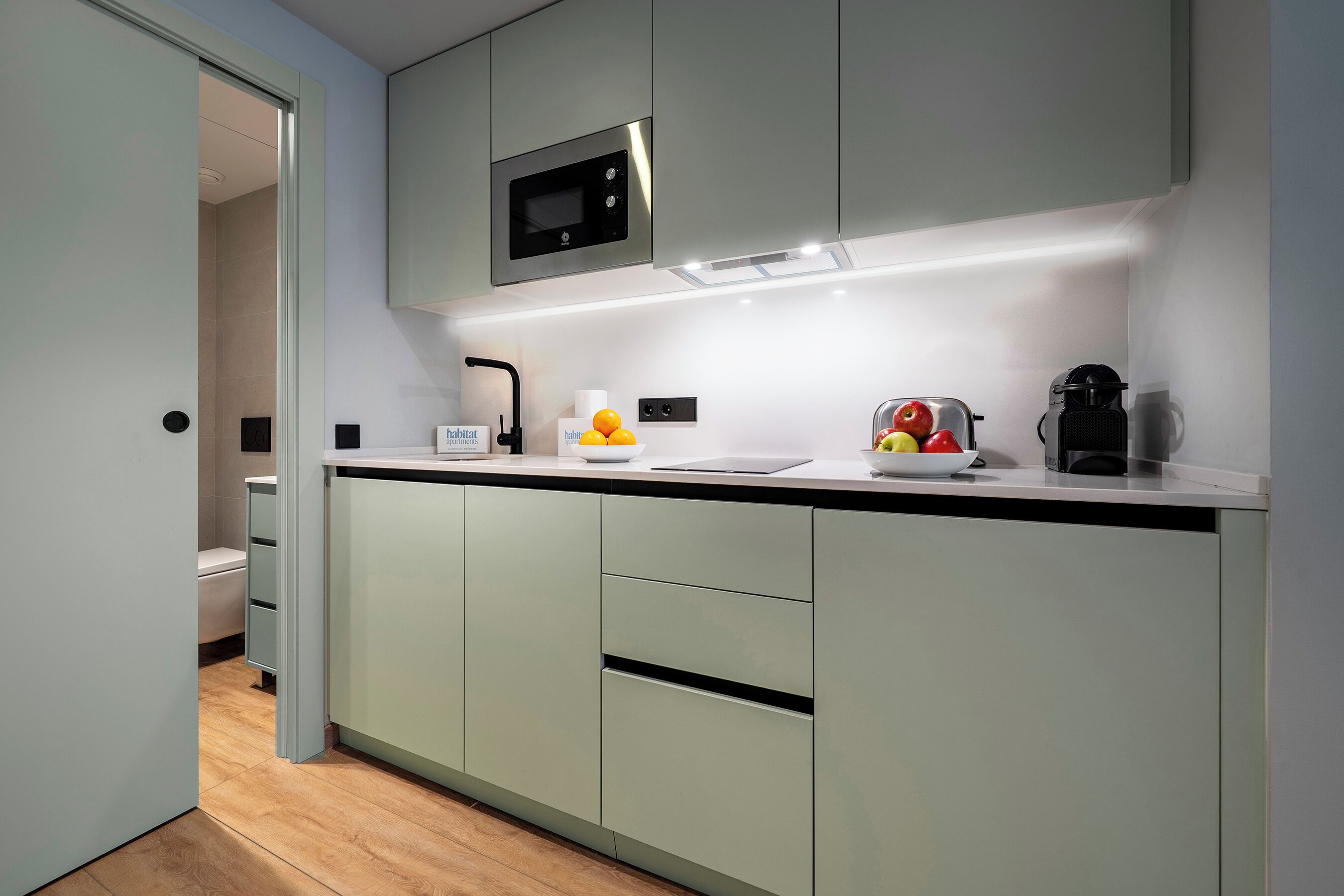 Una cocina moderna con microondas incorporado, cafetera y frutero en la encimera.