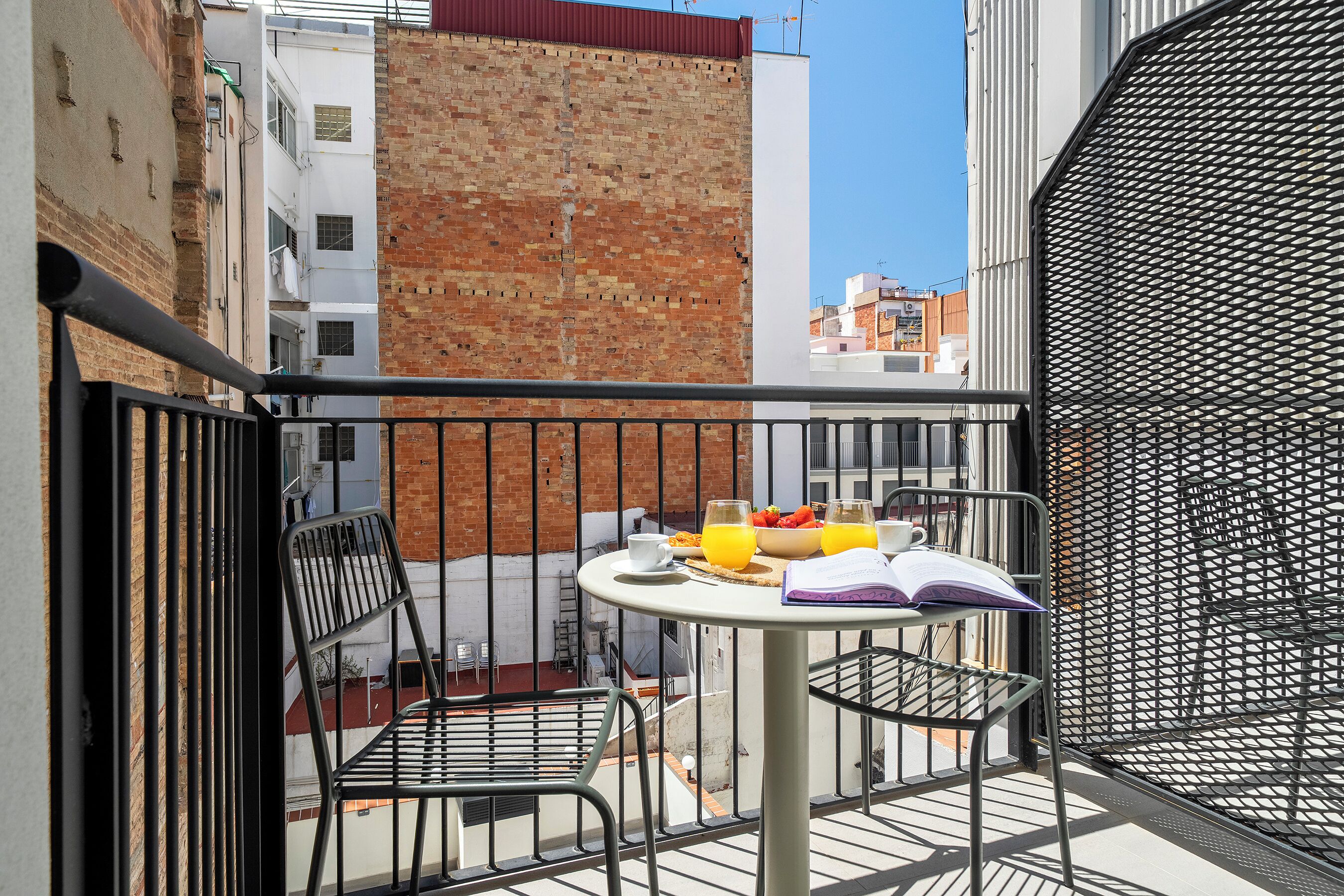 Een balkon met een tafel gedekt voor het ontbijt, inclusief een boek, een kopje en een schaal fruit.