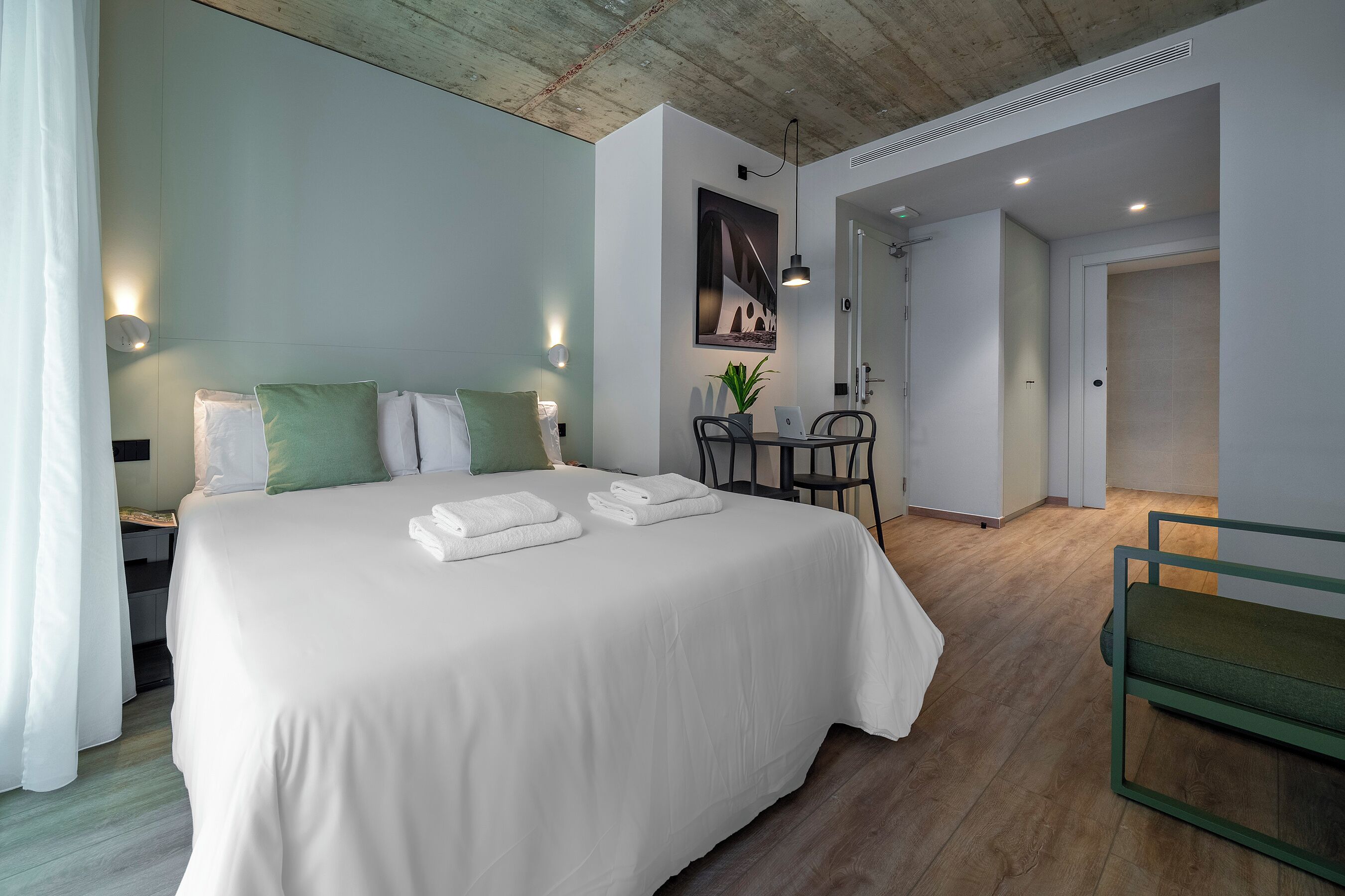 Et moderne hotelværelse med en stor seng, et skrivebord med en bærbar computer og et spiseområde.