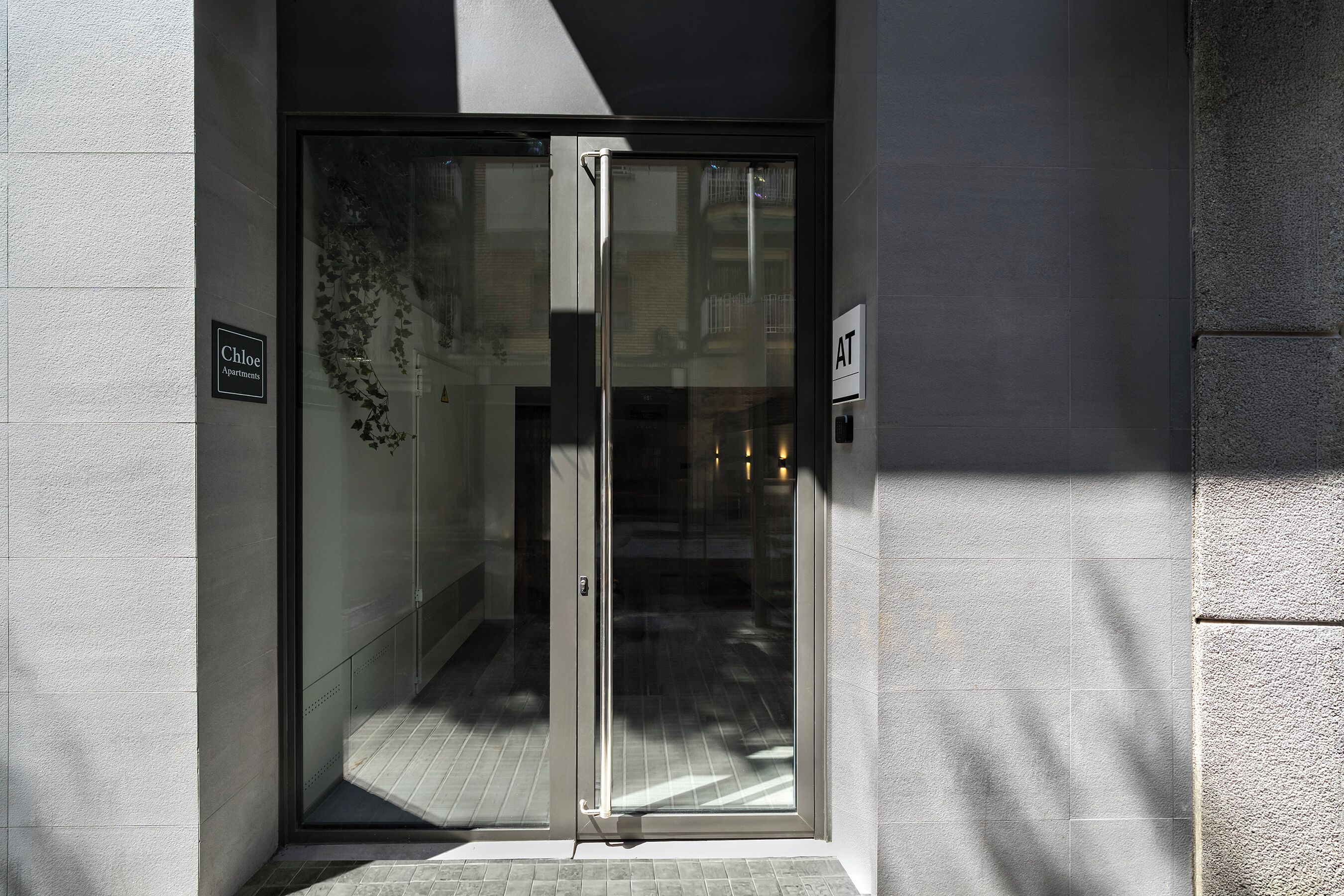 Ein moderner Gebäudeeingang mit Glastür, einem Schild mit der Aufschrift 'Chloe Apartments' und einem Keypad-Schloss.