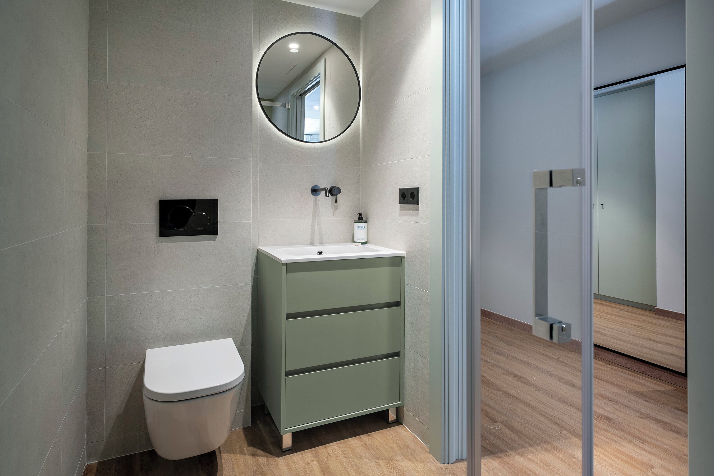 A modern bathroom with a toilet, a green cabinet, a mirror, and a shower area.