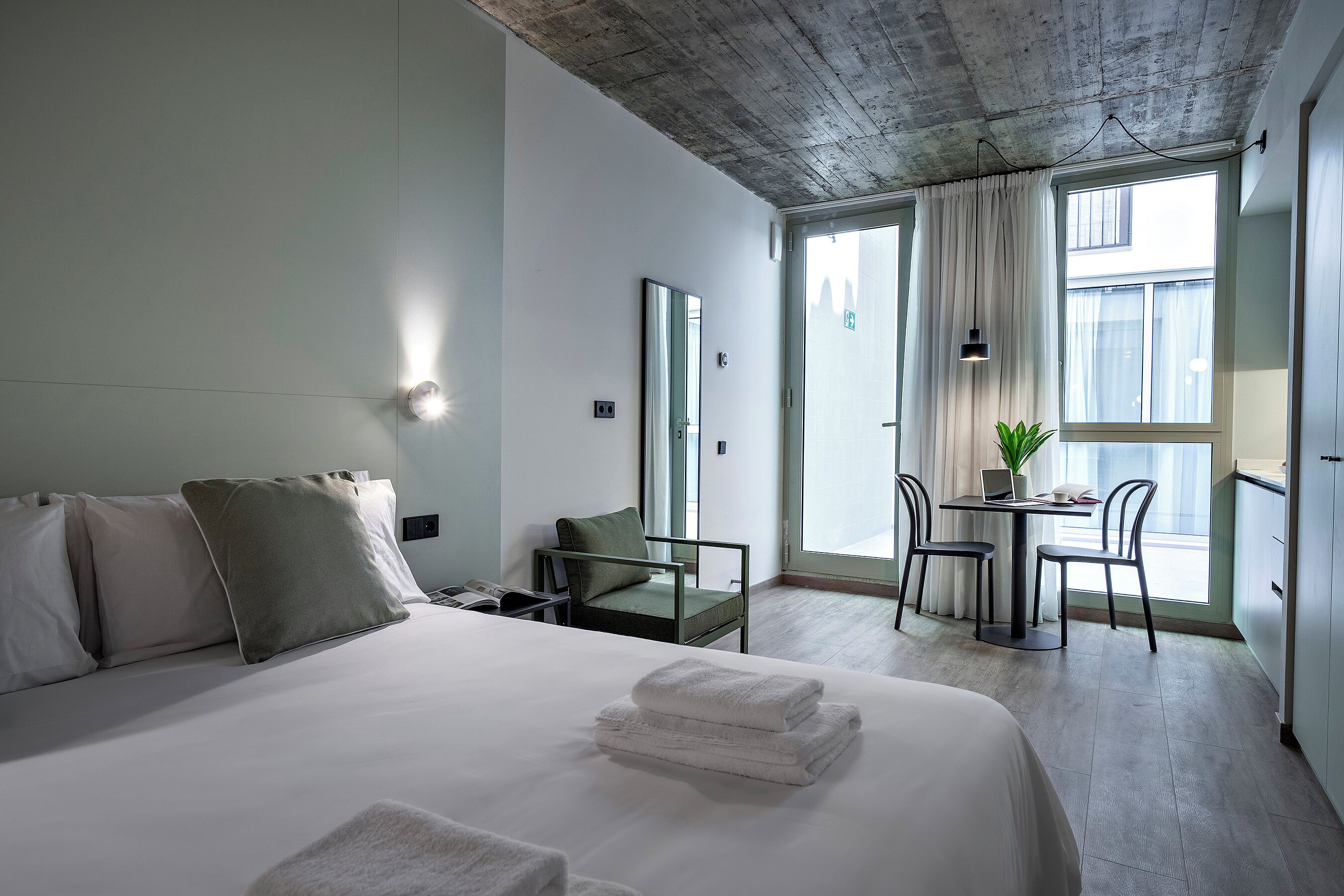 Ein Hotelzimmer mit einem Bett, einem Schreibtisch mit einem Laptop, einem Stuhl und einem Fenster mit Vorhängen.