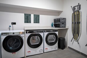 A laundry room with two front-loading washing machines, a dryer, and a wall-mounted ironing board. - Chloe Habitat Apartments (L'Hospitalet de Llobregat)