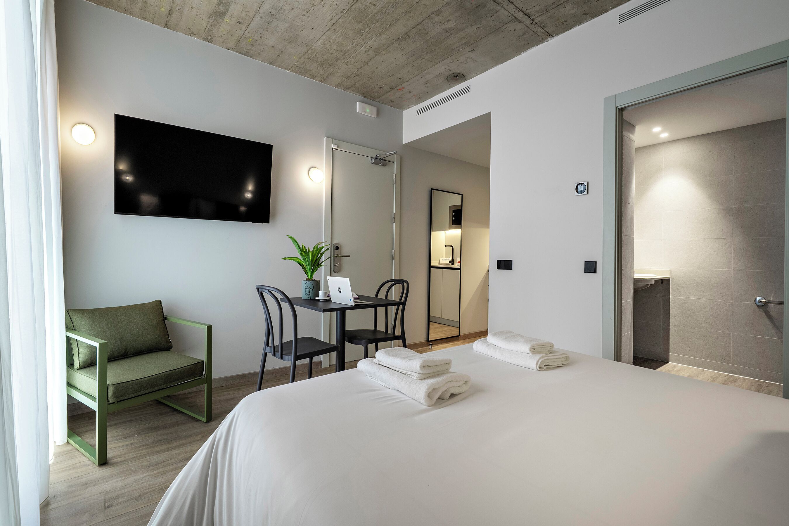 Habitación de hotel moderna con cama, escritorio, ordenador portátil, silla, televisor y baño.