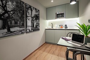 A modern kitchen with grey cabinets, a built-in microwave, and a dining area with a laptop and a plant. - Chloe Habitat Apartments (L'Hospitalet de Llobregat)
