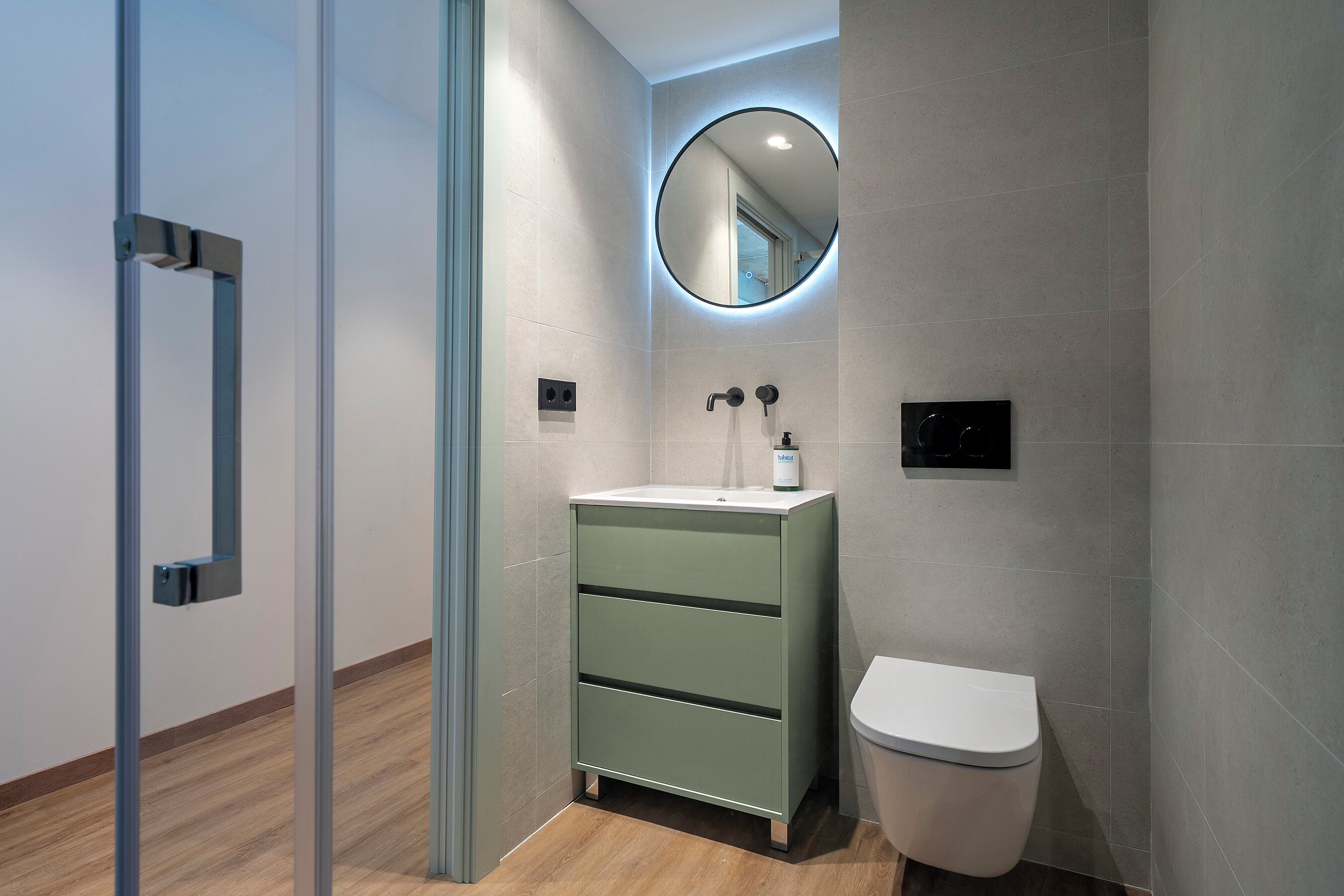 Un baño moderno con tocador verde, inodoro y espejo con luz circular.