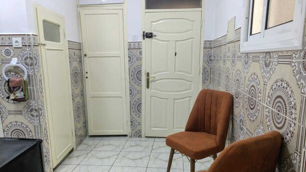 A small, tiled room with two brown chairs, a door, and patterned walls. - Mydar medina (Tanger)